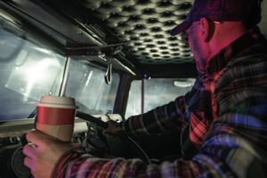 Trucker drinking coffee in the cab of his truck.